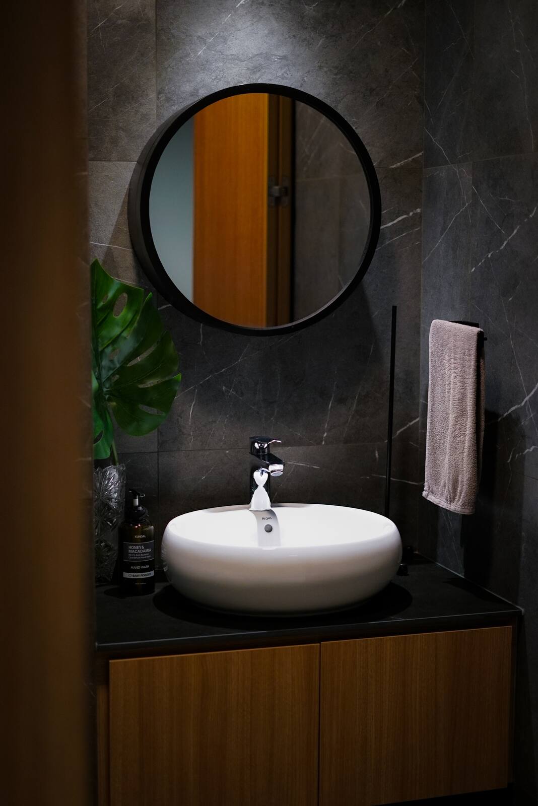 Bathroom with dark veined marble walls, a round black-framed mirror and a white vessel basin