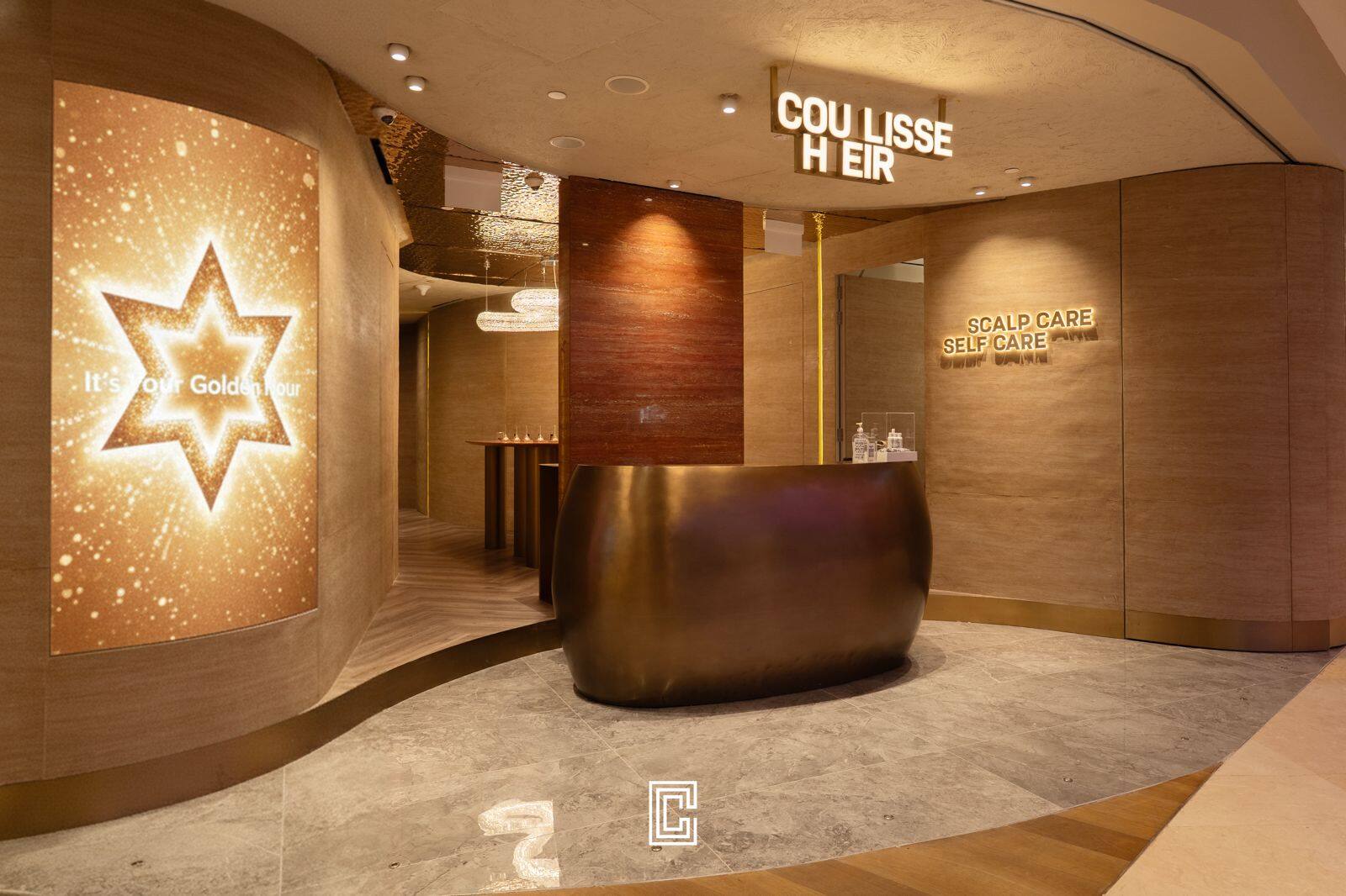 Salon reception with a sculptural bronze counter, curved timber walls and an illuminated starburst panel