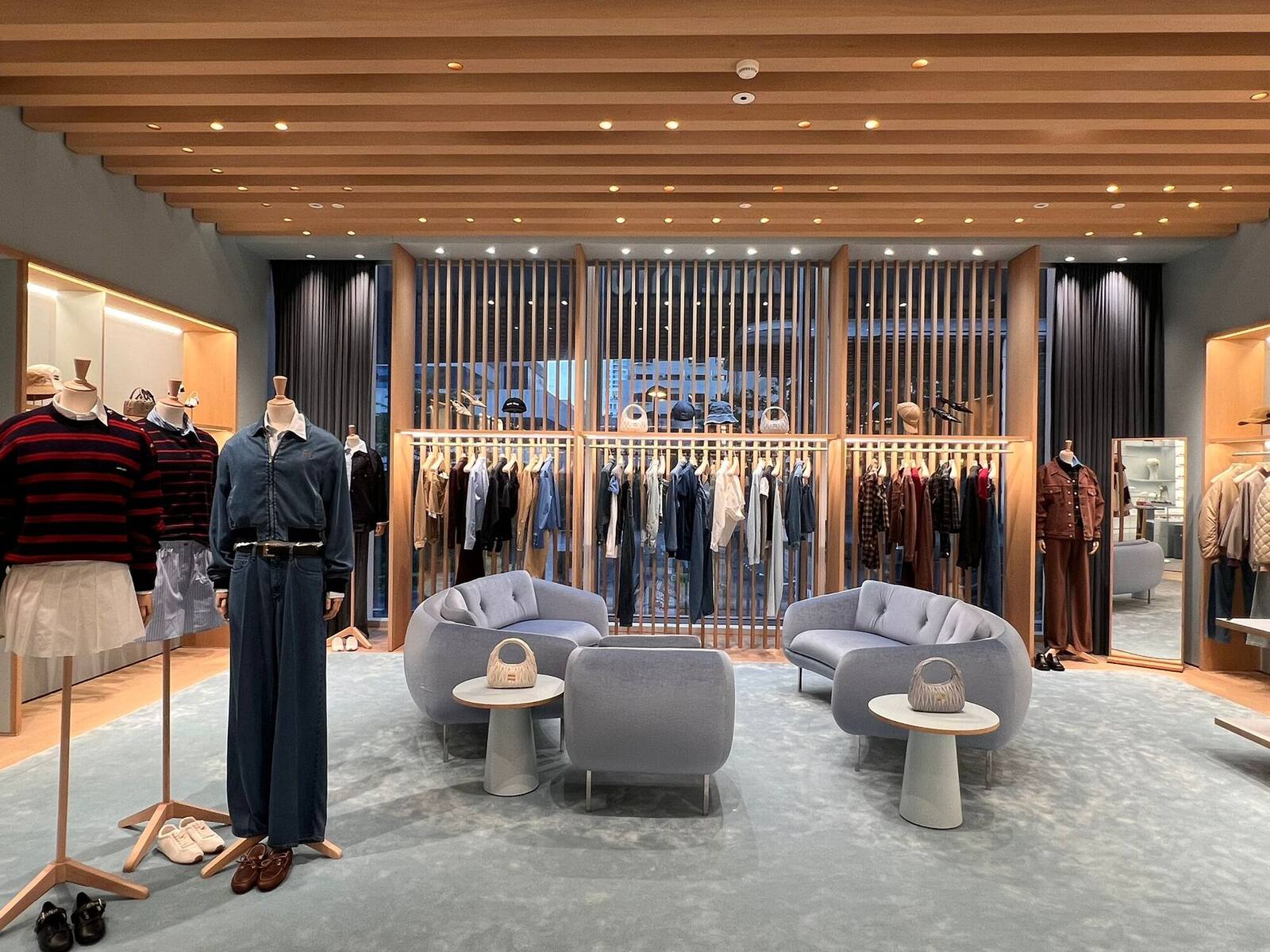 Boutique interior with mannequins, a timber fin screen and rounded grey lounge seating on a pale rug