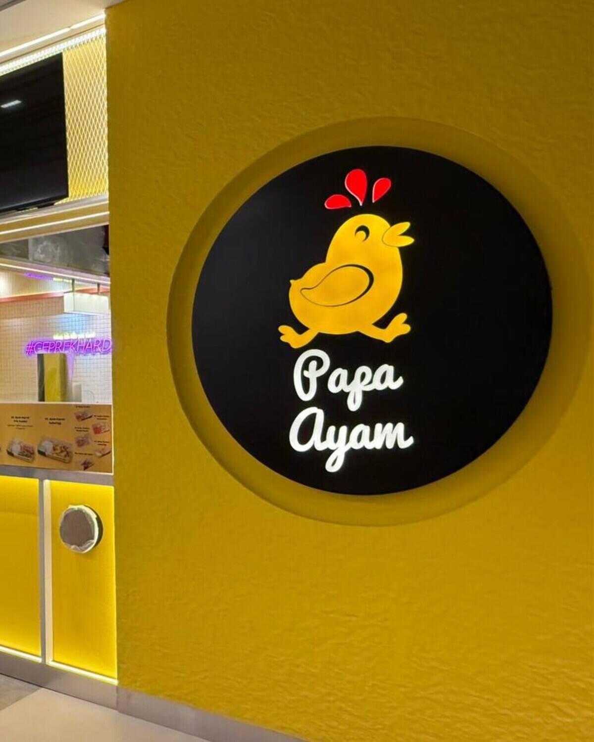 Yellow food-and-beverage counter with a large illuminated circular brand panel and overhead menu screens