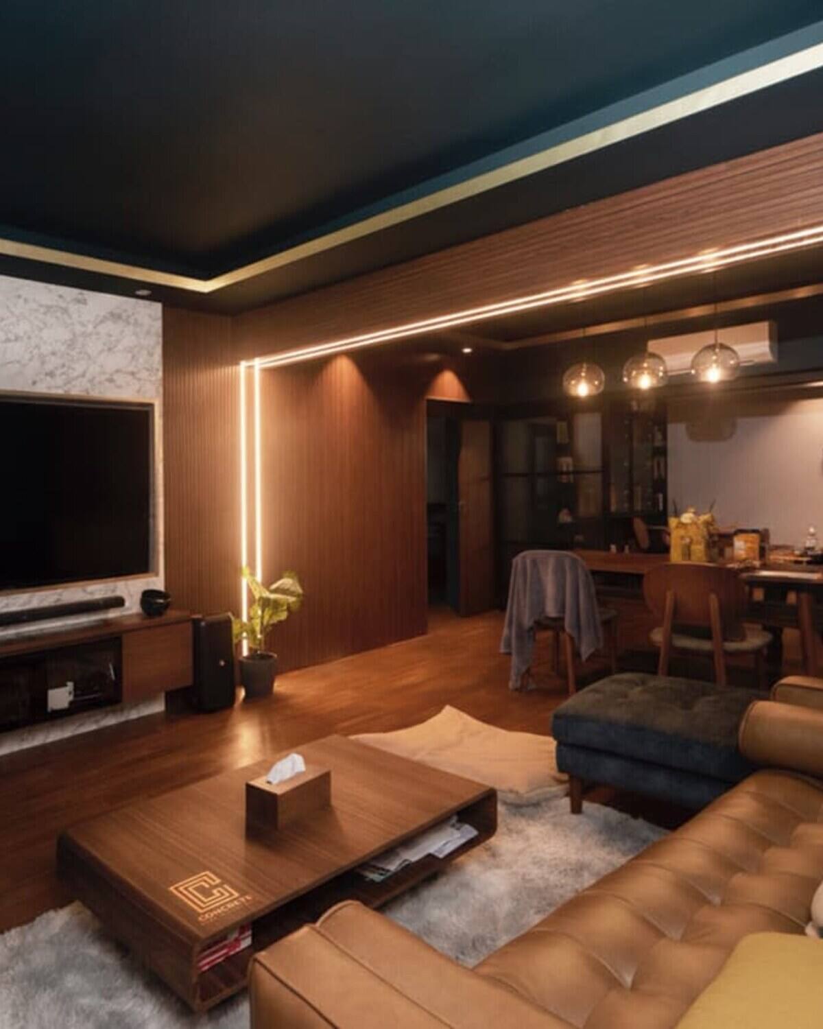 Living and dining area with a teal ceiling trimmed in gold, a marble television feature wall, fluted walnut panelling and a mustard leather sectional