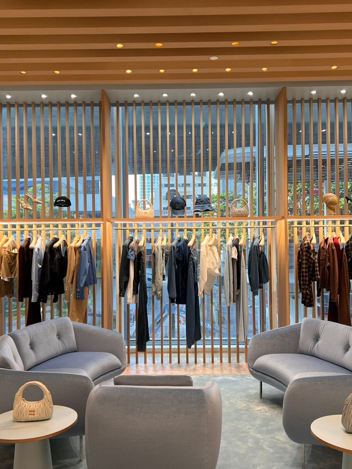 Boutique interior with clothing rails set behind a timber fin screen, mannequins and pale grey lounge seating