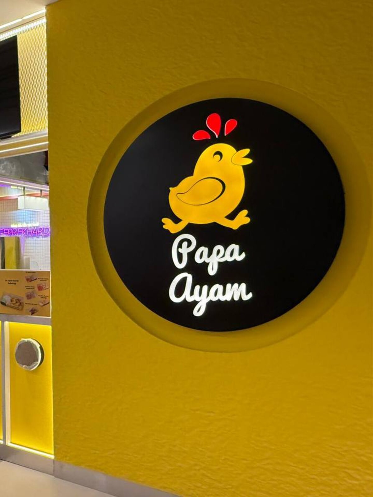 Yellow food-and-beverage counter with a large illuminated circular brand panel and overhead menu screens