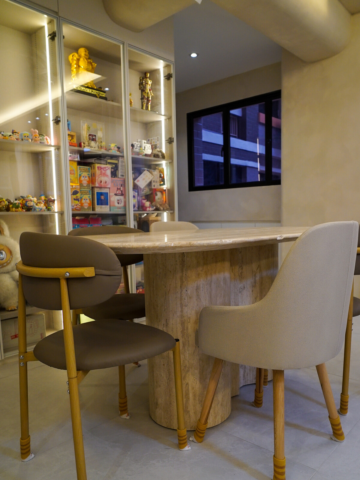 Dining nook with a stone-topped table, brass-legged upholstered chairs and lit display shelving