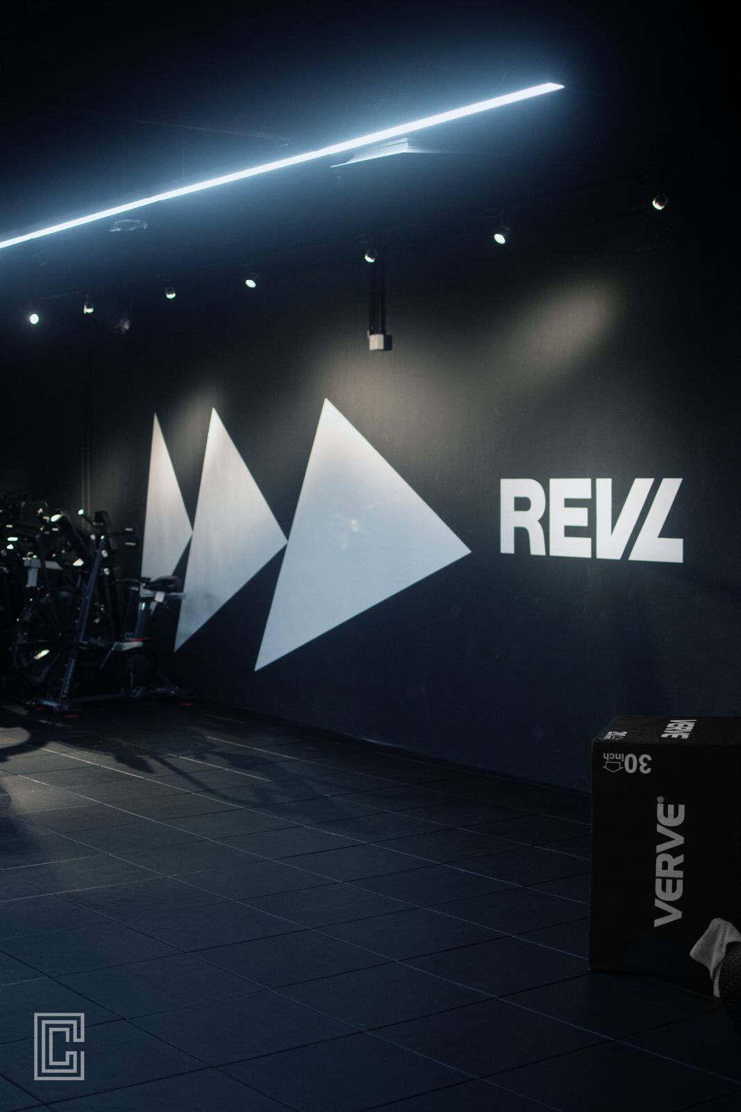 Dark fitness studio with a large white brand mark lit against a matte black wall