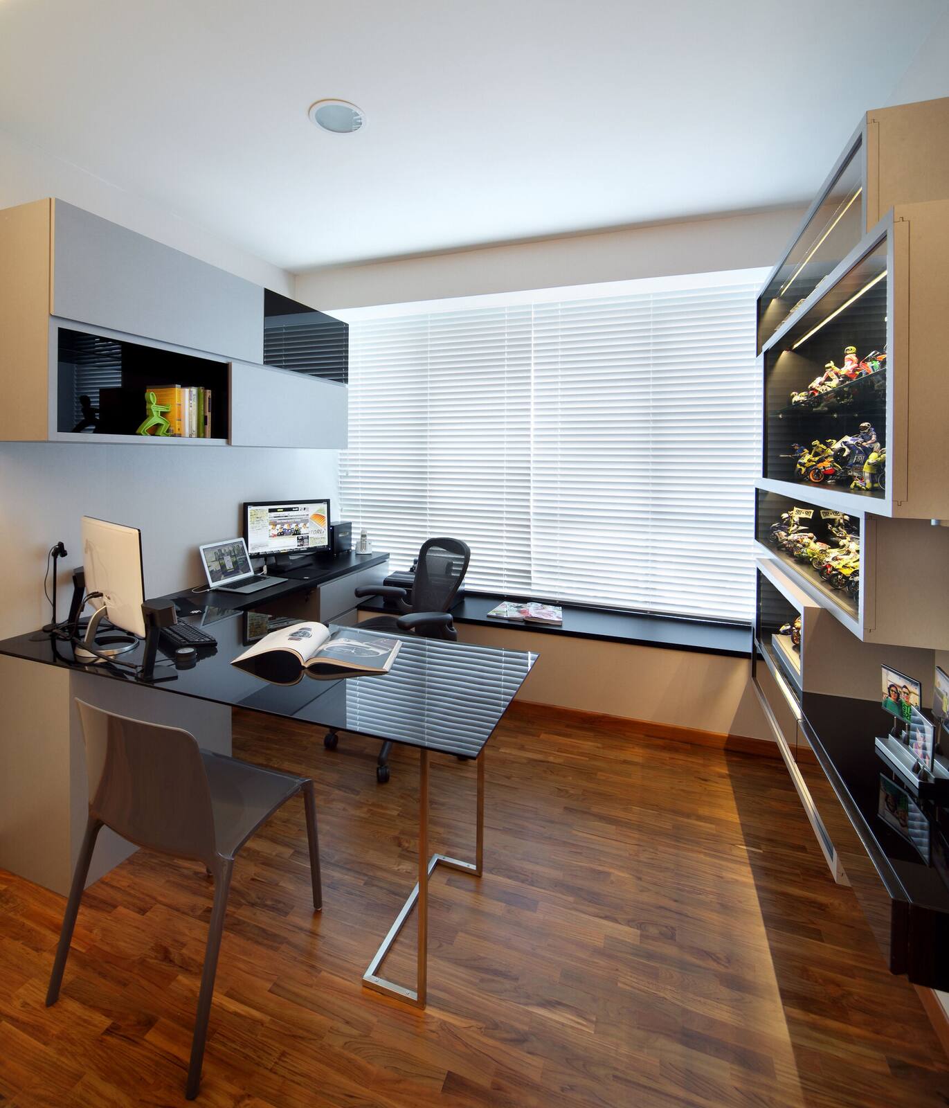 Home study with a dark built-in shelving wall, a glass-topped desk and venetian blinds