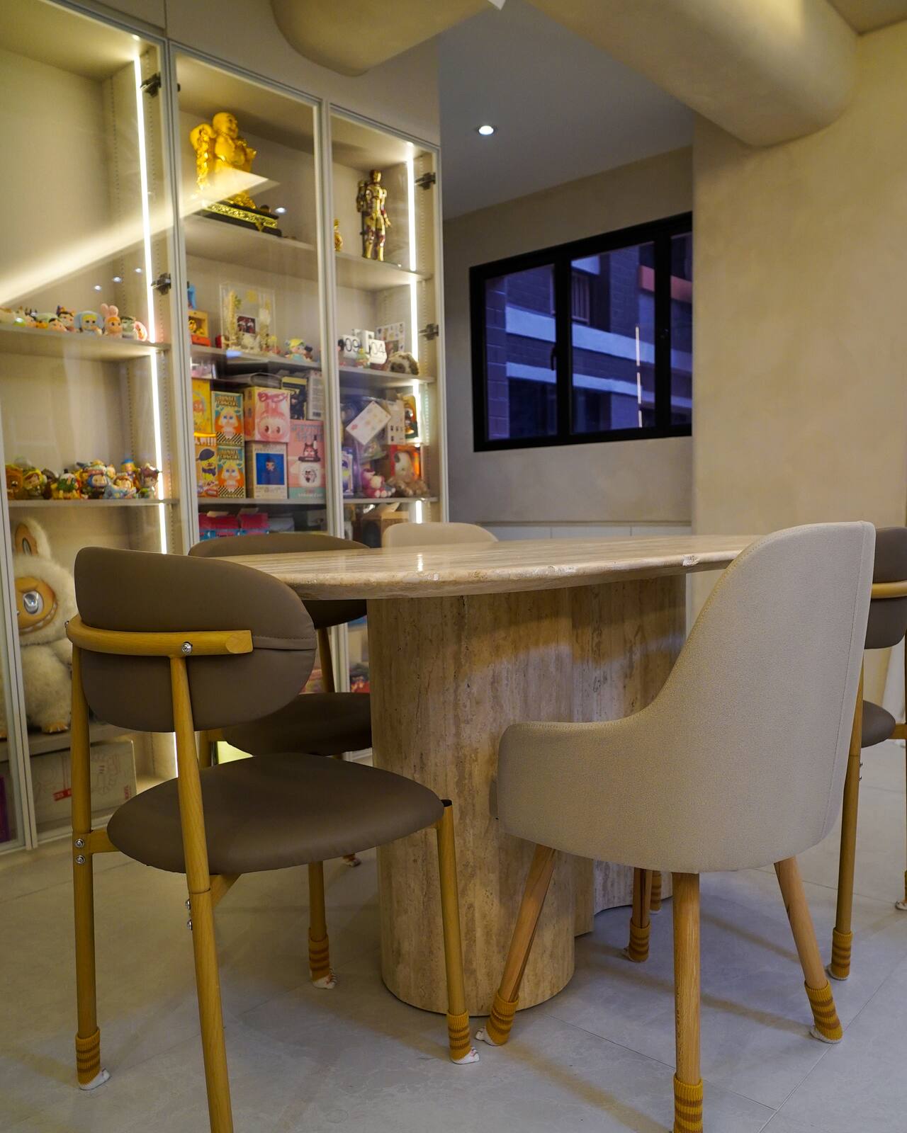 Dining nook with a stone-topped table, brass-legged upholstered chairs and lit display shelving